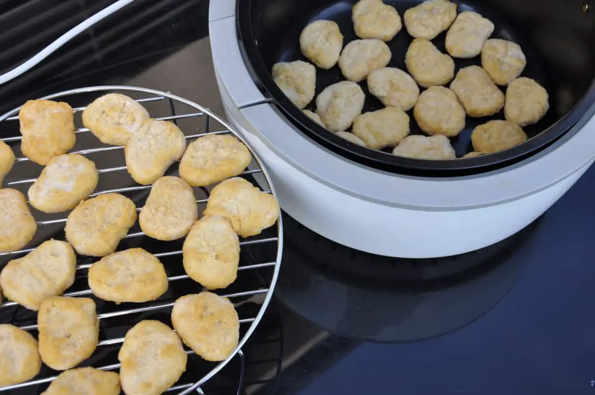 Stacked chicken nuggets on a rack and in the basket of an air fryer